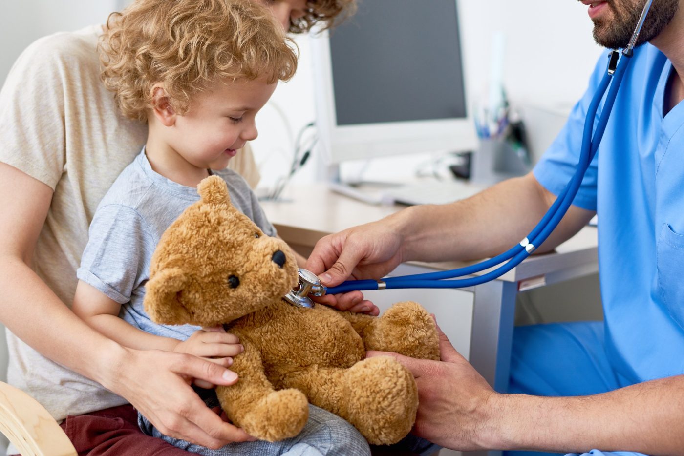 A physician listens to a child's teddy bear with a stethoscope